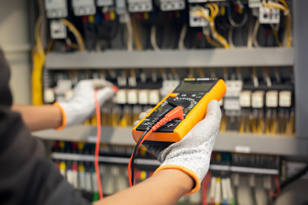 electrician engineer uses a multimeter to test the electrical installation and power line current in an electrical system control cabinet.